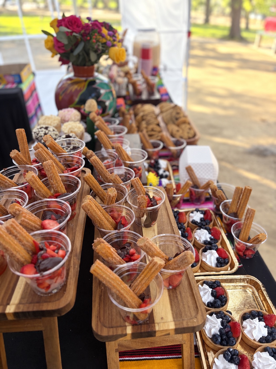 Rows of dessert cups filled with churros, strawberries and cream, set out on wooden risers at an outdoor event.