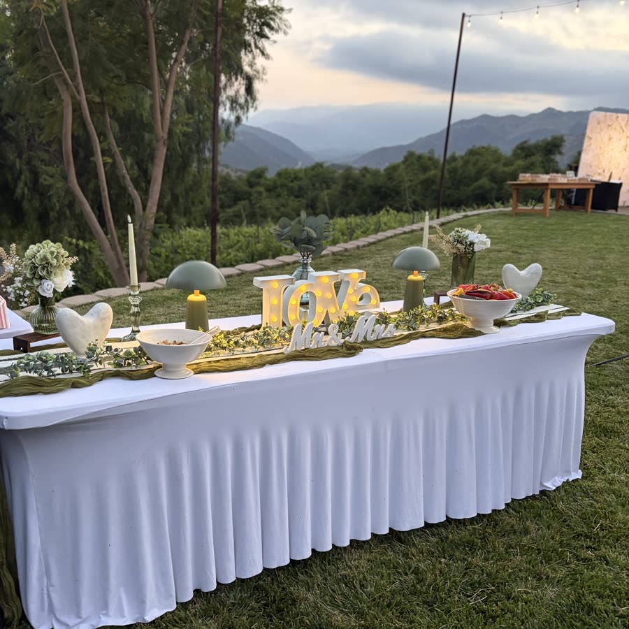 An outdoor wedding table at golden hour with a lit love sign, candles and greenery.