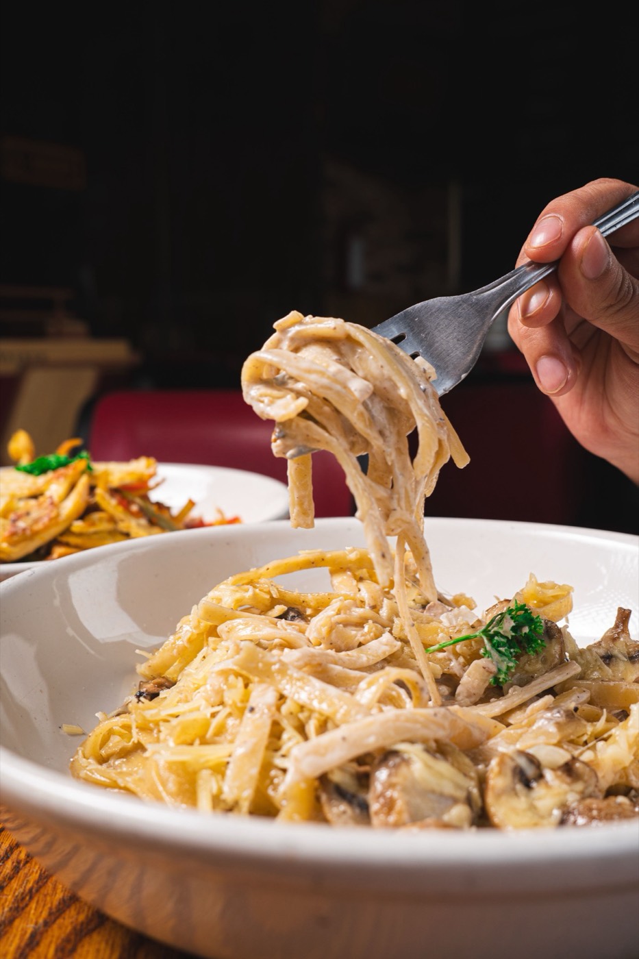A forkful of fettuccine in cream sauce lifted from a bowl of pasta and mushrooms.