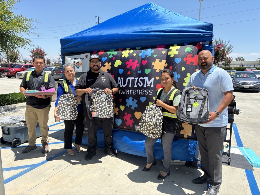 A family standing at the J and J booth under a blue canopy with an autism awareness banner.