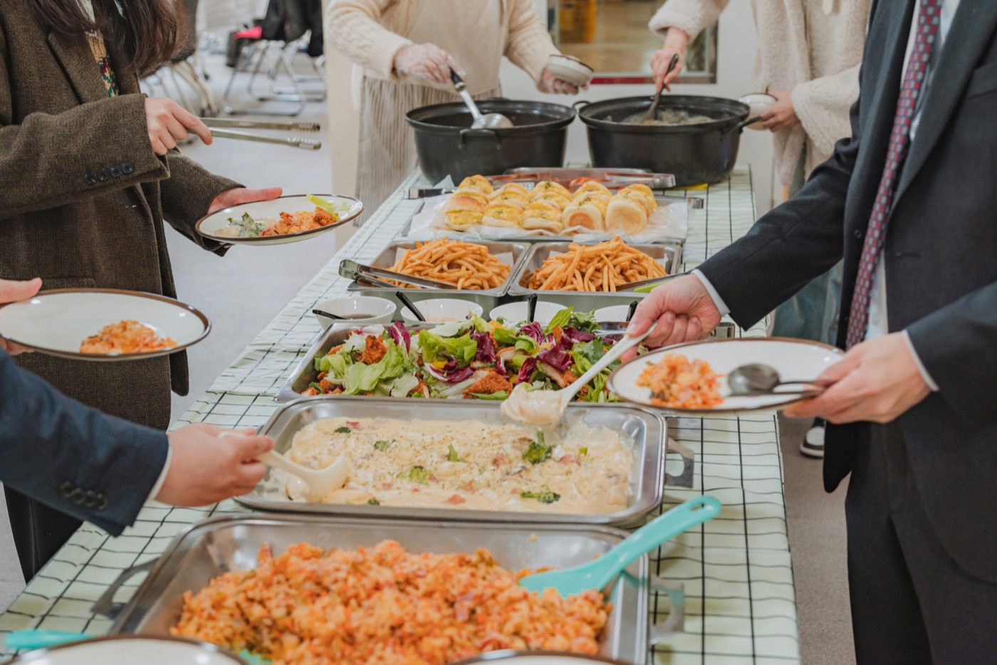 Guests in business dress serving themselves along a hot buffet line of pasta, rice and salad.